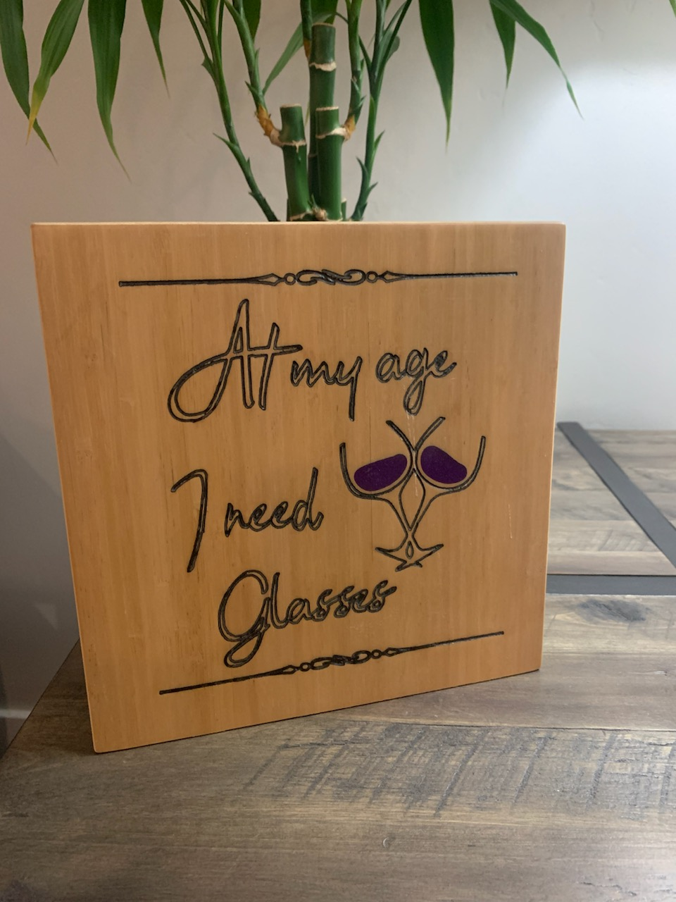 Wood sign engraved with 'At my age I need Glasses' and a wine glass design, alternate angle