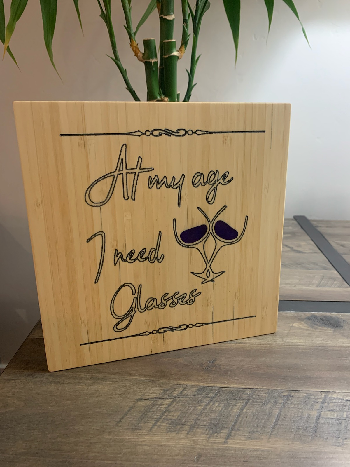 Wood sign engraved with 'At my age I need Glasses' and a wine glass design