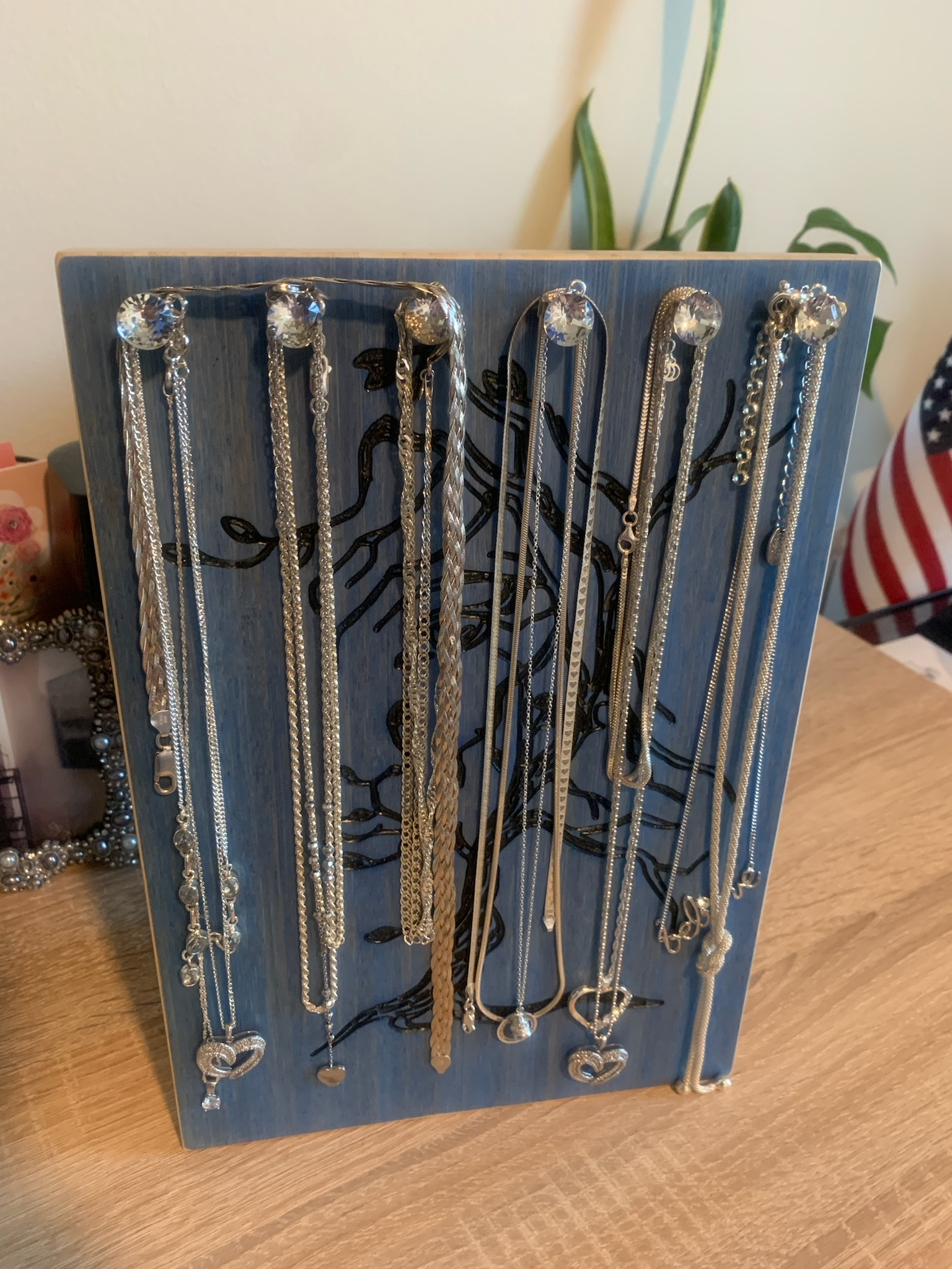 Blue-stained wood jewelry holder with laser-carved tree design, holding necklaces